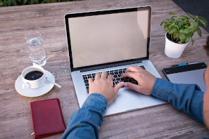 Hands typing on keyboard with computer screen in front